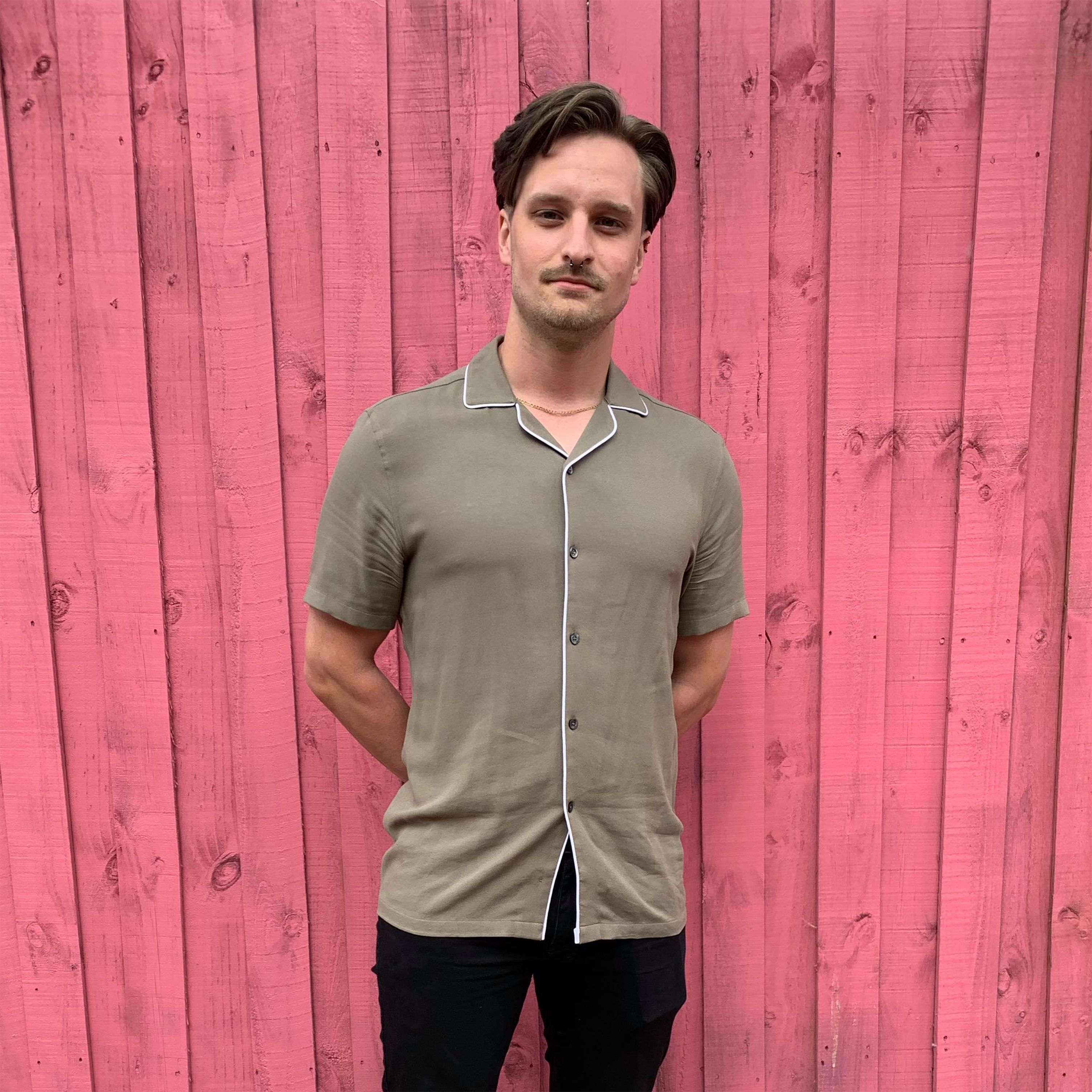 Pink timber background with man standing in brown shirt and black pants